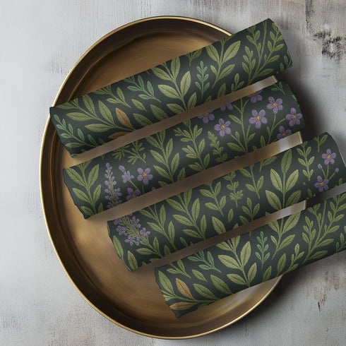 A 4-piece cloth napkin set featuring embroidered-style botanical illustrations of wildflowers and herbs in shades of gold, mint, and lavender on a dark green background; made from soft polyester, square-shaped, with a luxe and mystical design.